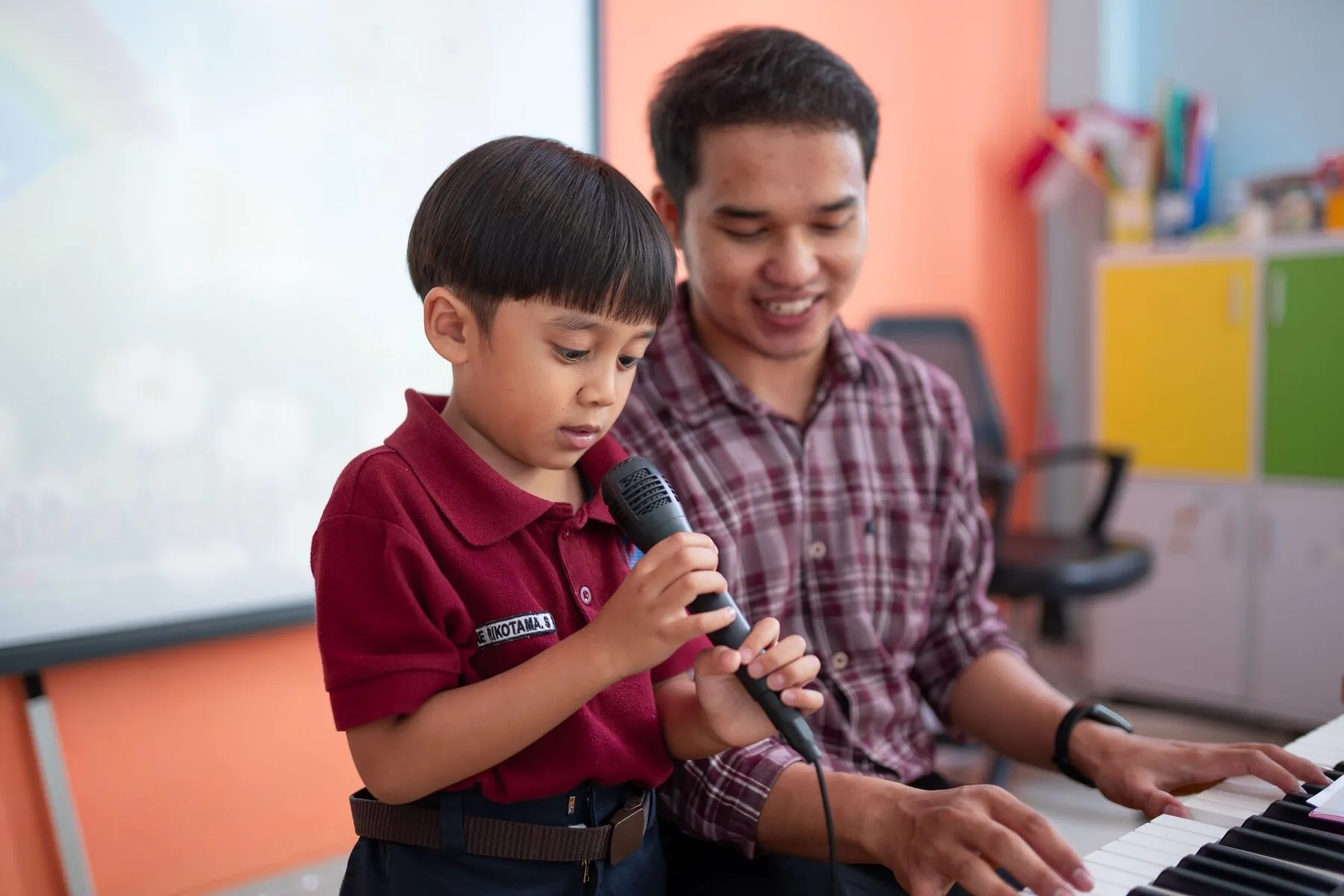 Siswa bernyanyi dengan mikrofon diiringi guru bermain piano